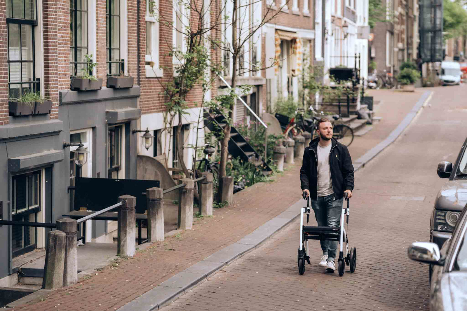 A man walks along a street with a 'Rollz Motion' walking frame.