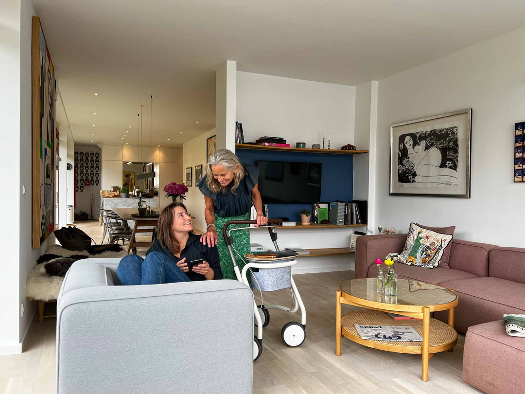 A woman stands with her 'byACRE' indoor walker and laughs with her daughter in a loungeroom