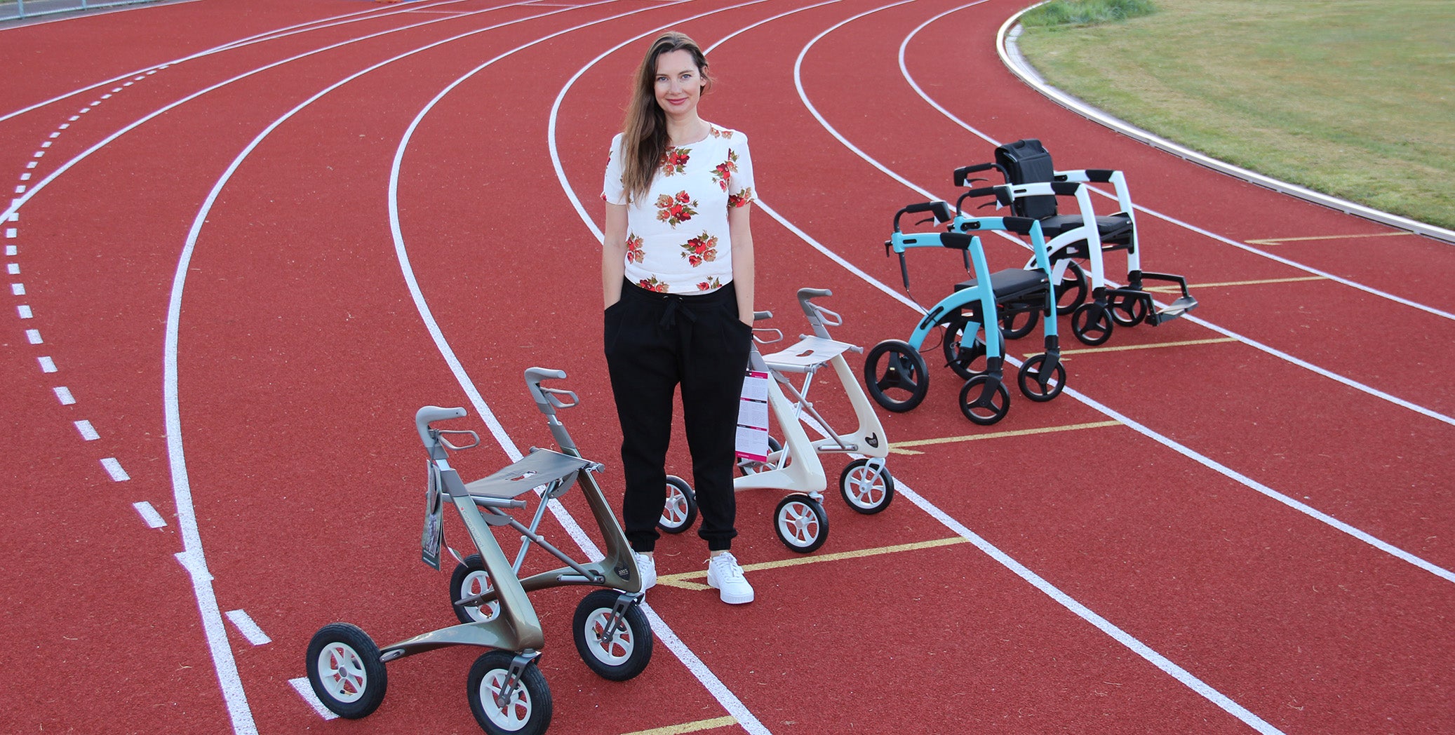 Anna Wallace stands on a running track with four modern walking frames on display.