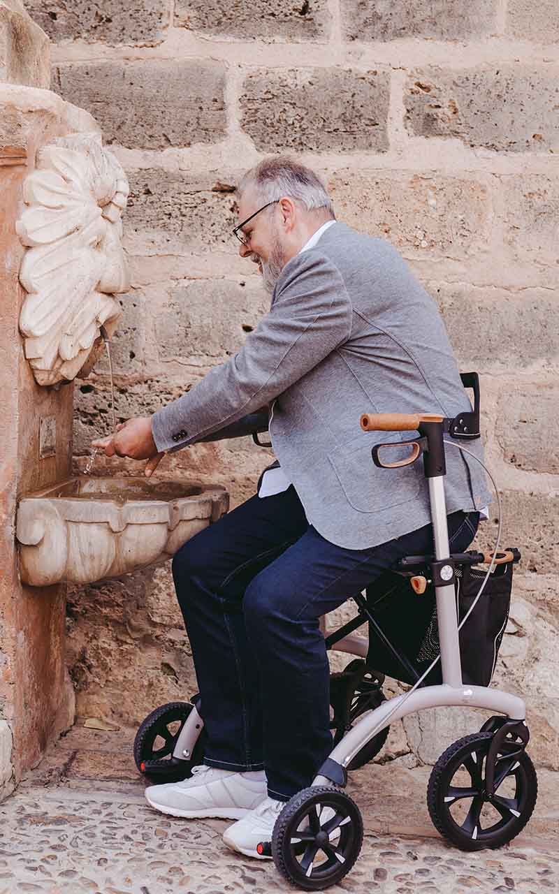 A man sits on a Saljol walking frame washing his hands in a fountain