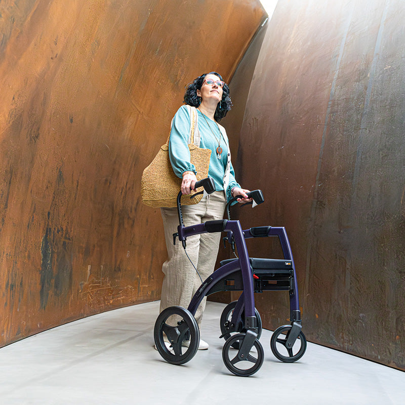 A woman stands in front of an artistic sculpture using a Rollz Motion walker for support