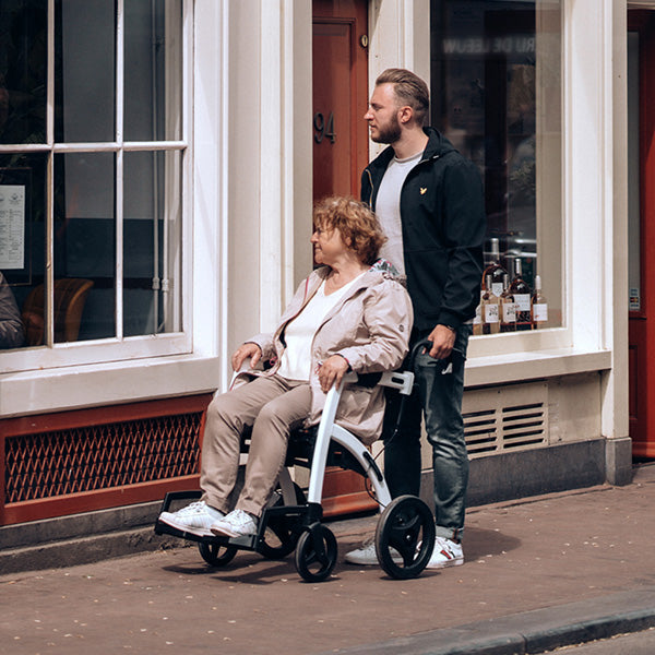 A woman sits in a 'Rollz Motion' wheelchair while being pushed along a footpath by her adult son