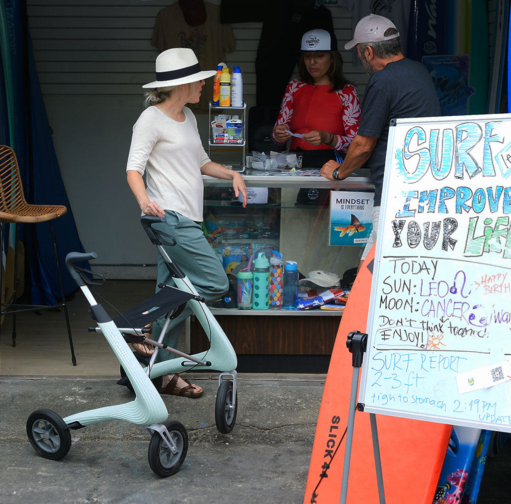 A woman is supported by a modern byACRE rollator at a surf shop