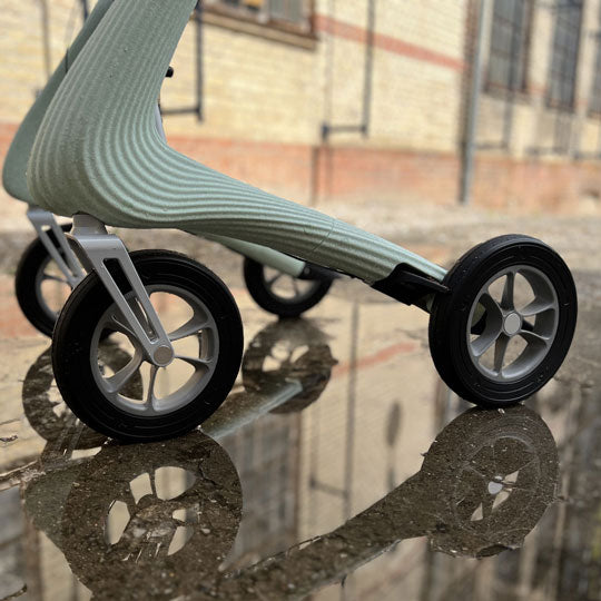 A close up of the wheels on a byACRE Nordic Pioneer rollator on a wet footpath