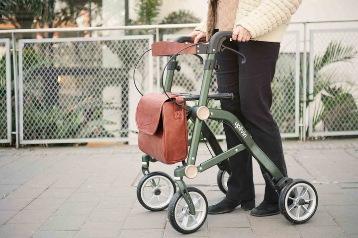 A close up shot of the 'Uplivin Trive' walker rollator being used by a person on a brick footpath.