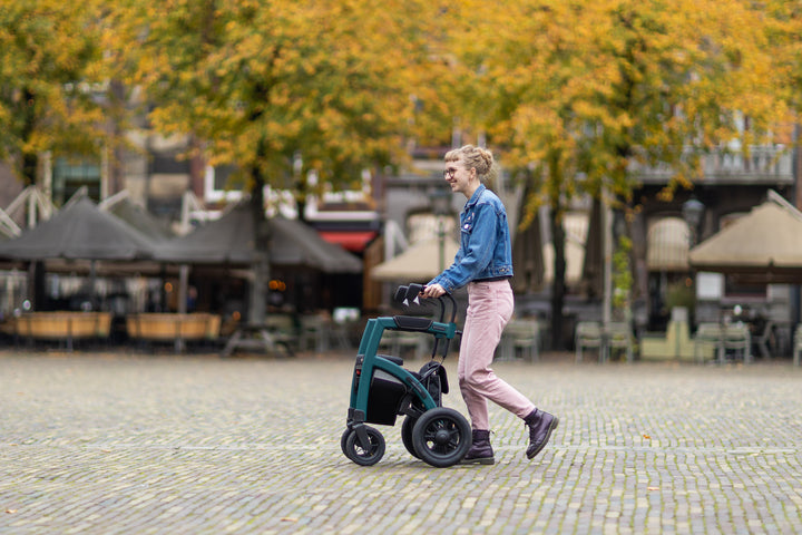 A girl walks across a town square using a 'Rollz Motion Performance' rollator with gazebos in the background