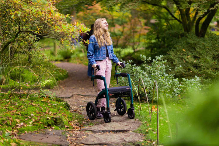 A girl walks down a path in a park using a 'Rollz Motion Performance' walking frame