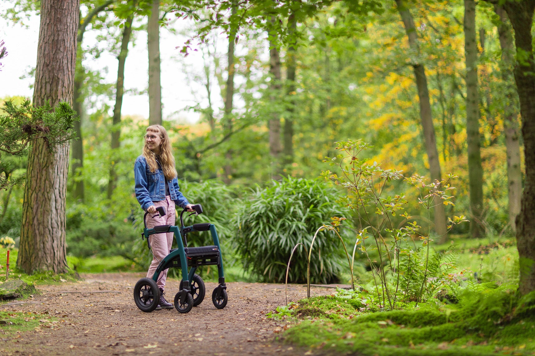 A girl smiles as she uses a 'Rollz Performance' walking frame in a park with trees in the background