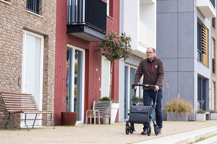 A man walks on a footpath with the 'Rollz Flex' walking frame with apartments in the background