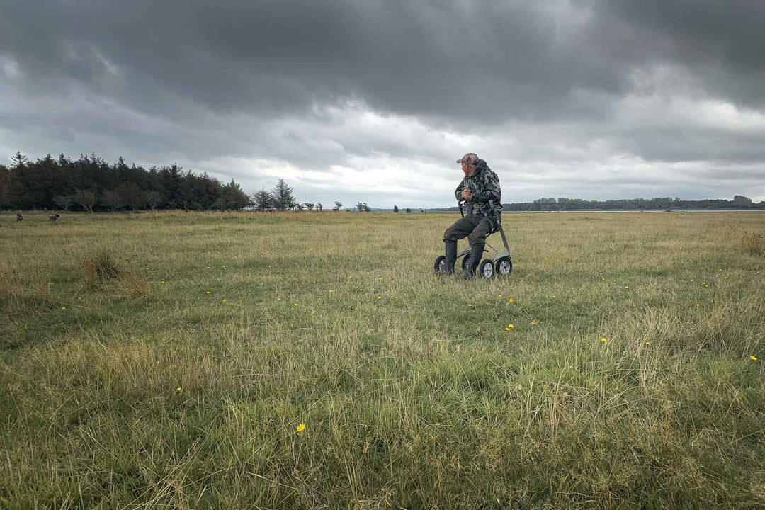 A man sits on a 'byACRE Carbon Overland' walker in the middle of a grassy field beneath a sky filled with dark clouds 