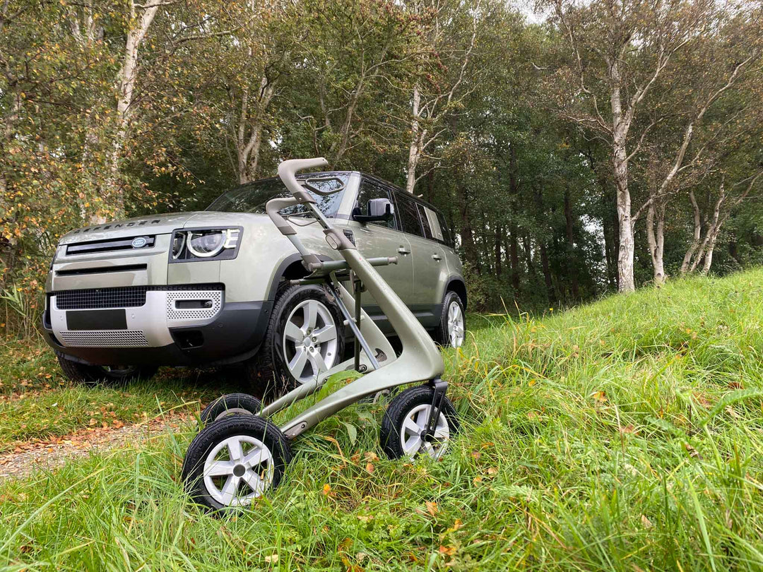 'byACRE Carbon Overland' walking frame with 'Land Rover Defender' in a grassy field with trees in the background