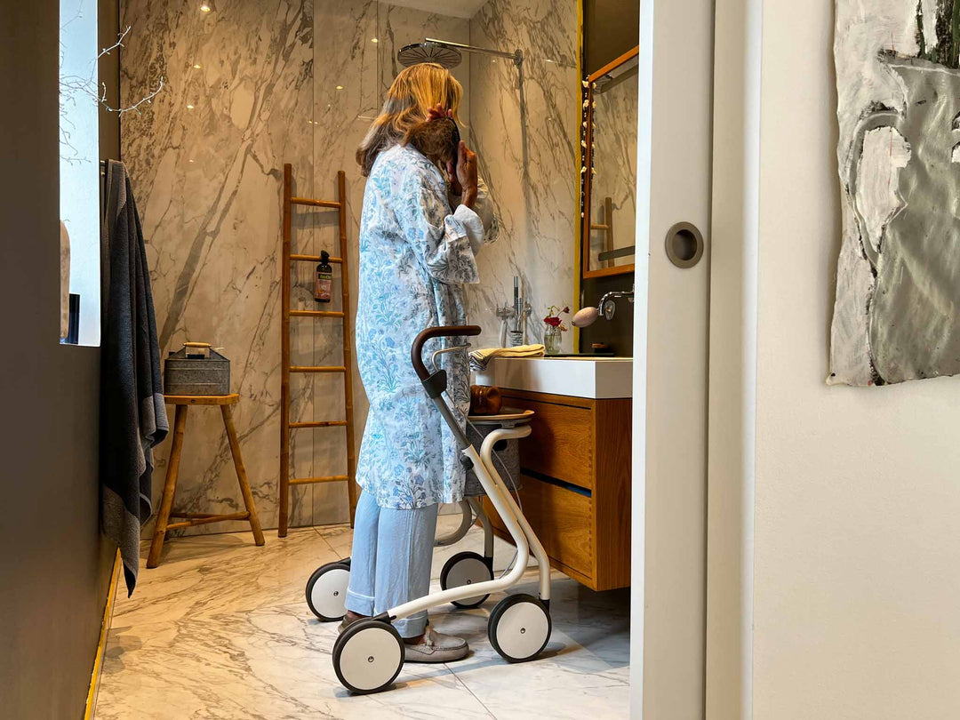 A woman stands in her modern bathroom using the 'byACRE Scandinavian Butler' indoor walking frame, looking in the mirror