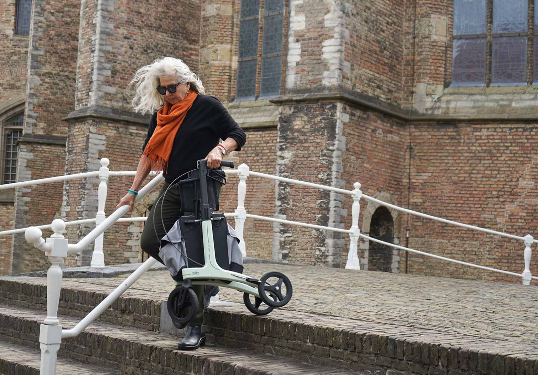 Person carrying a light weight mobility walker on steps in front of a brick building