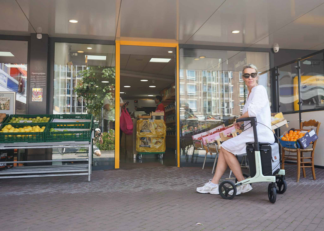 Woman sits on a light weight walker outside a store with fruit displays.