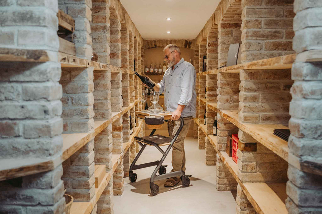 Man uses a Saljol Indoor Walking Frame while looking at a bottle of wine in a cellar.