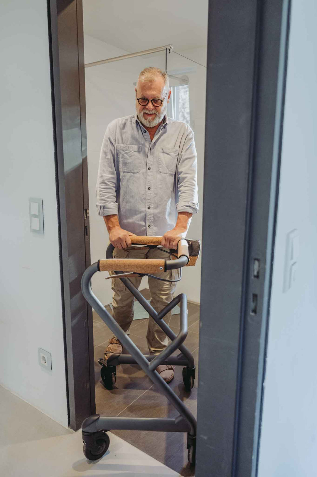 A man walks through a narrow bathroom doorway using a Saljol Indoor Walker Rollator