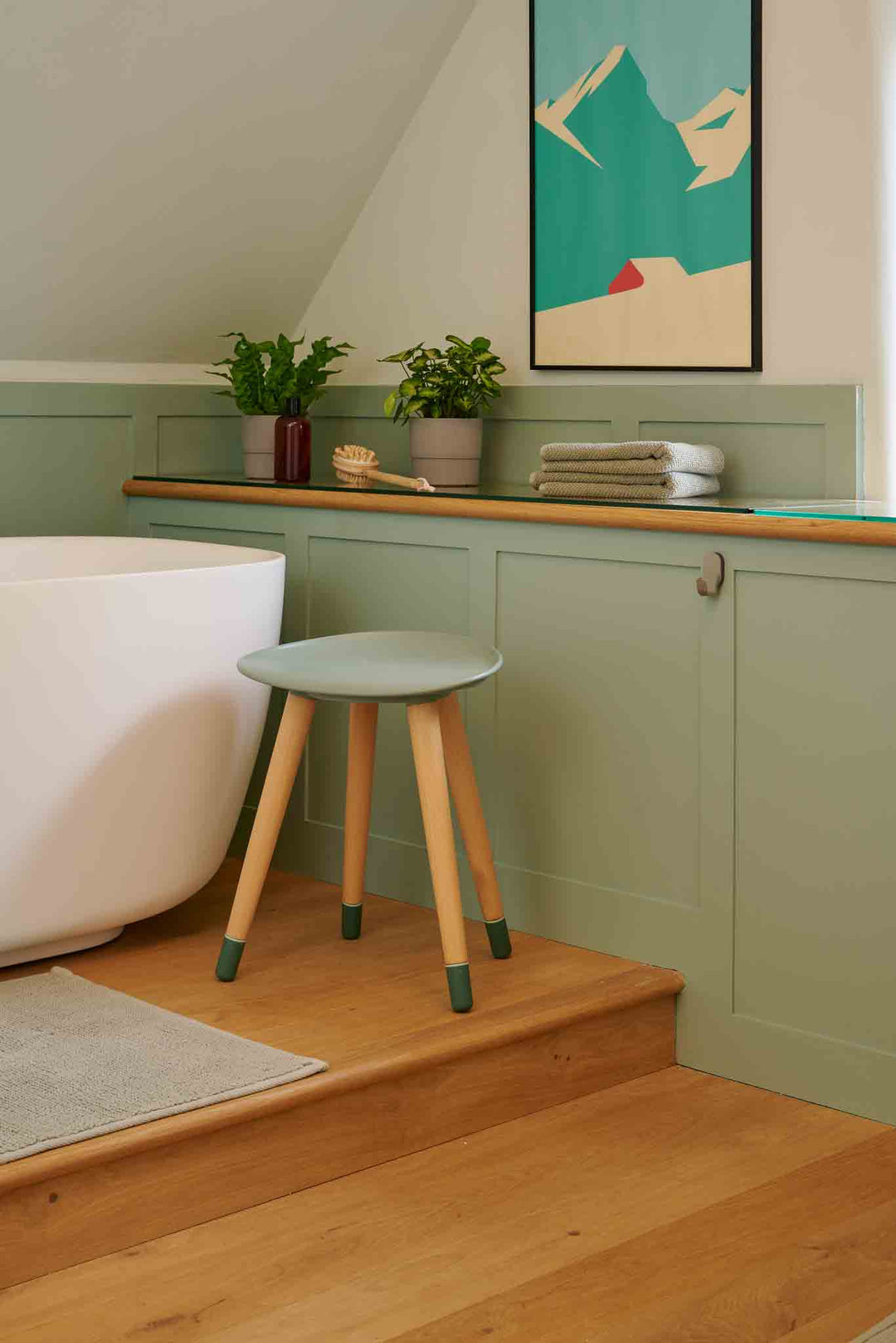 Bathroom with a stool, bathtub, and framed artwork on a green wall.