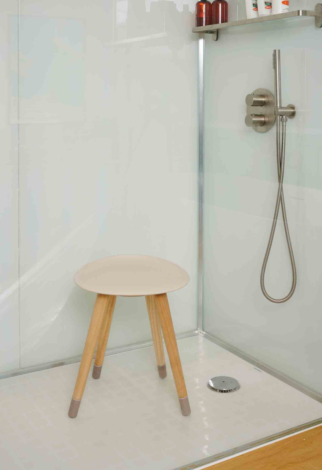 Small shower stool with steel legs with wooden finish and a beige seat in a bathroom setting.