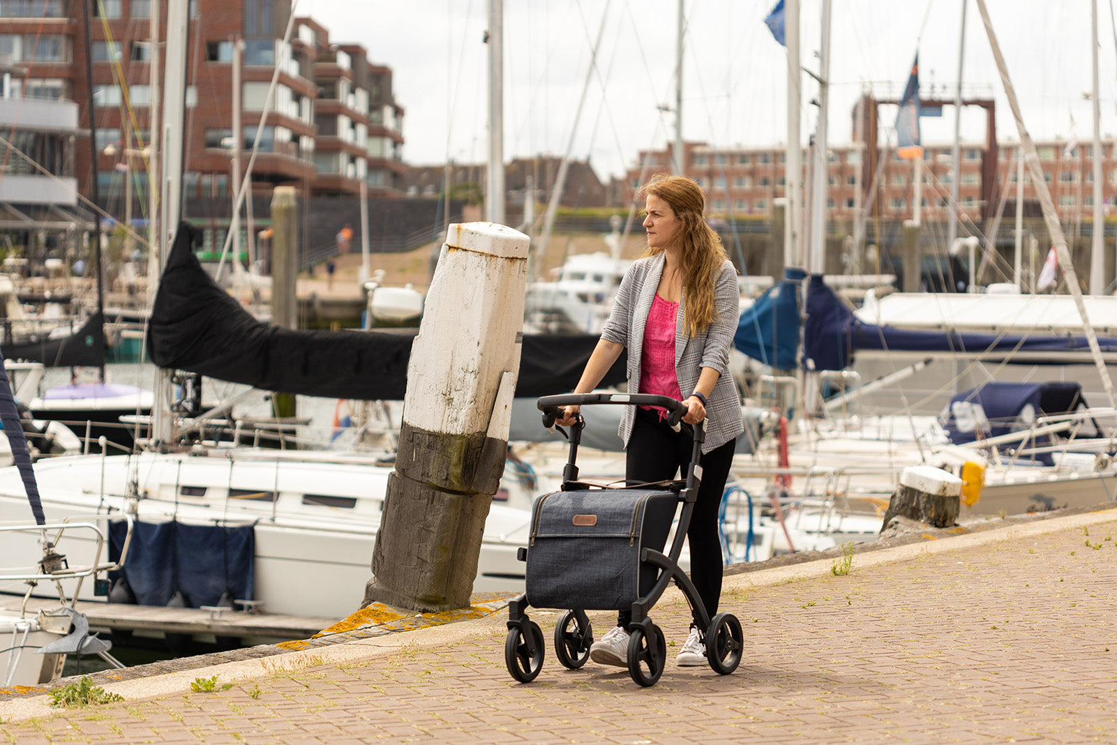 A young woman walks along dock side with the Rollz Flex Walker Rollator with boats in the background.