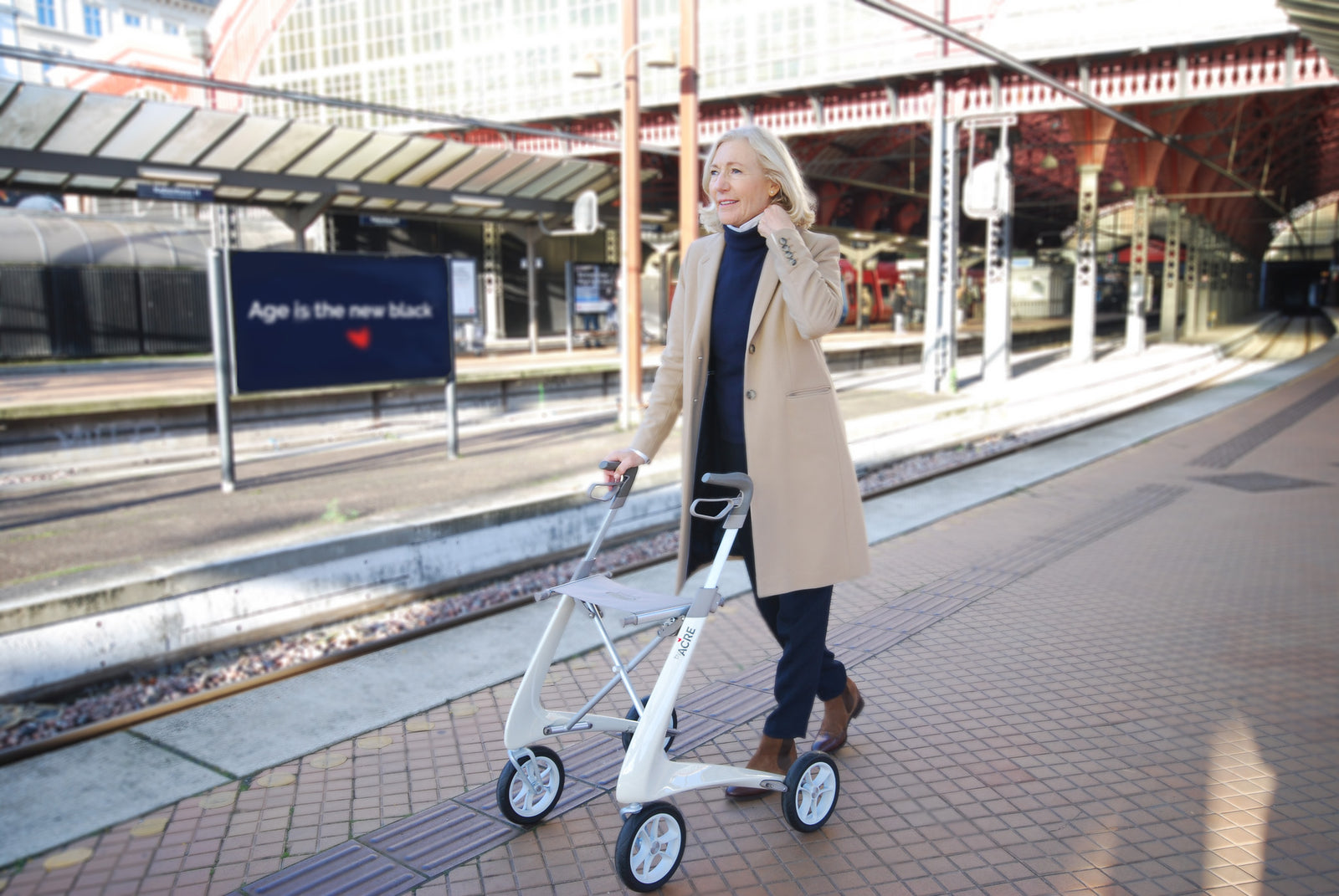 A woman walks along a train station platform with a modern byACRE walking frame