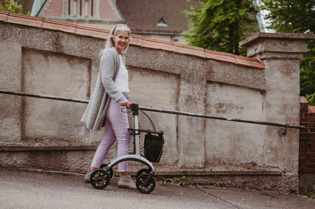A woman walks down a footpath while using a Saljol Carbon Fibre Rollator