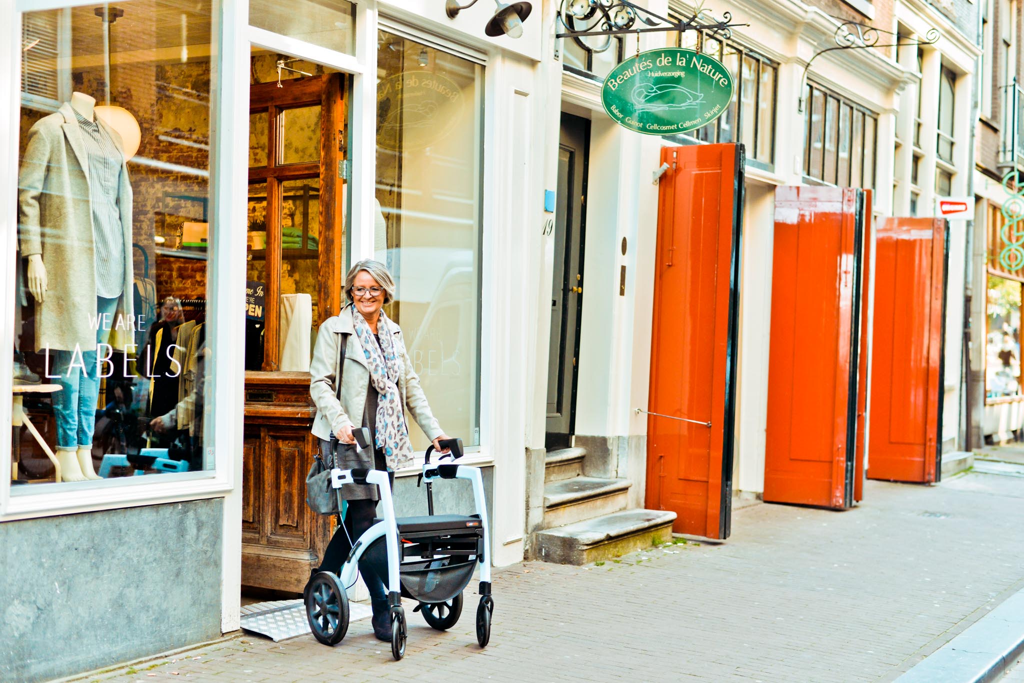 A smiling woman is walking out of a shop using the Rollz Motion walker rollator